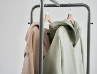 Close-up of pastel hoodies hanging on a minimalist clothes rack with a gray background.