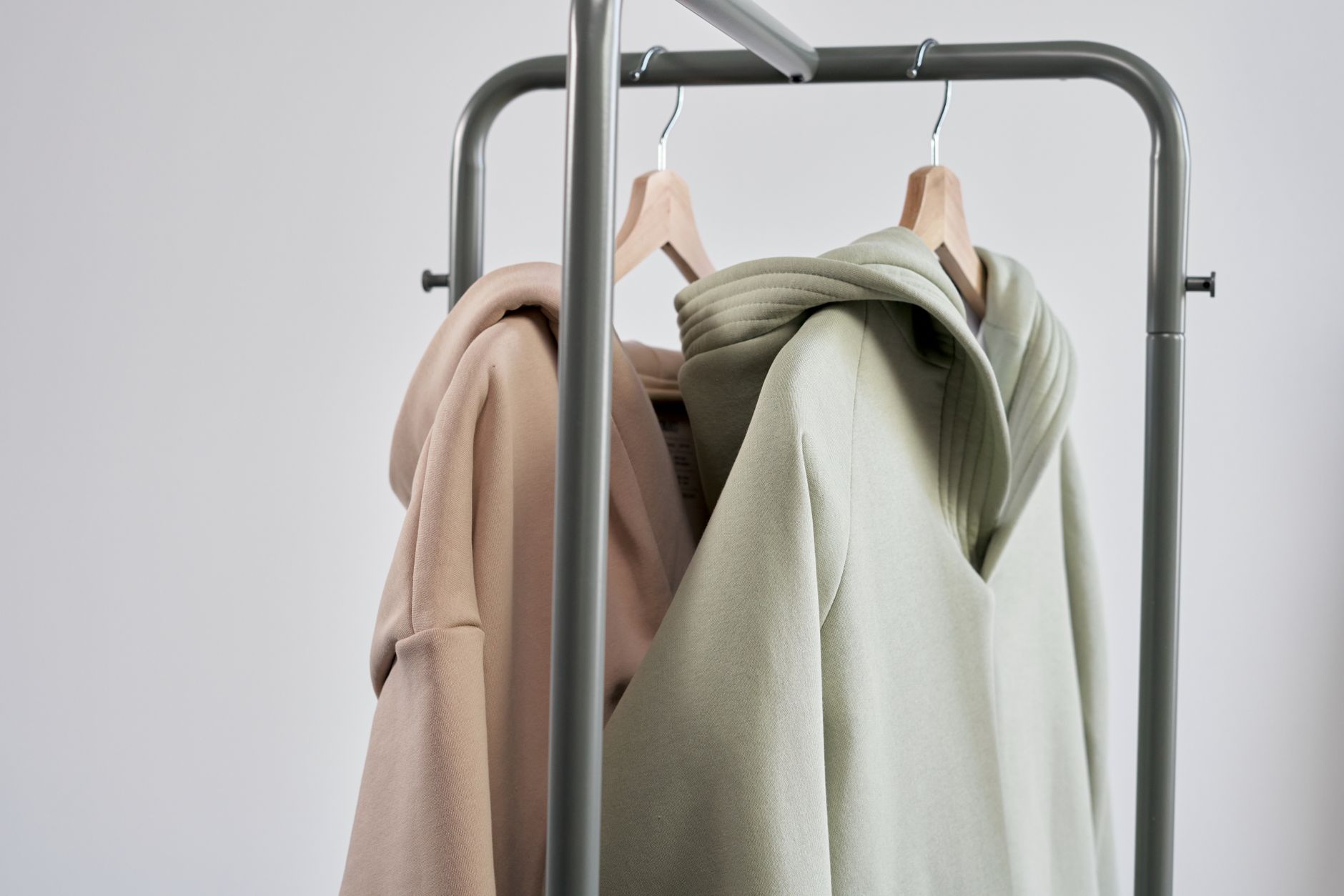 Close-up of pastel hoodies hanging on a minimalist clothes rack with a gray background.